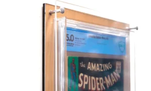 Photograph focusing on the top of the Crafti Comics UV-FLEX Display Case with light wood backing. Frame for displaying graded comic books. 99% UV-protected, museum-quality acrylic standard. Hangs portrait or landscape with twin engraved mounting holes. Crafti's laser-cut layered designs provide depth without creating pressure.
